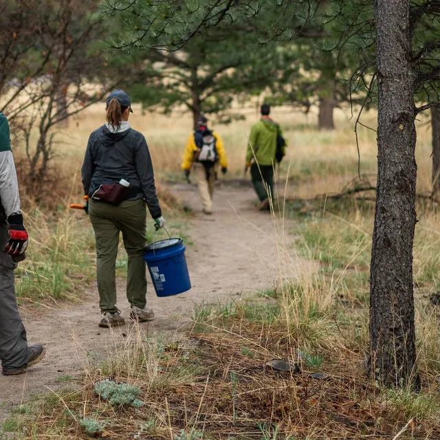 Volunteers carrying tools and a bucket along a park trail